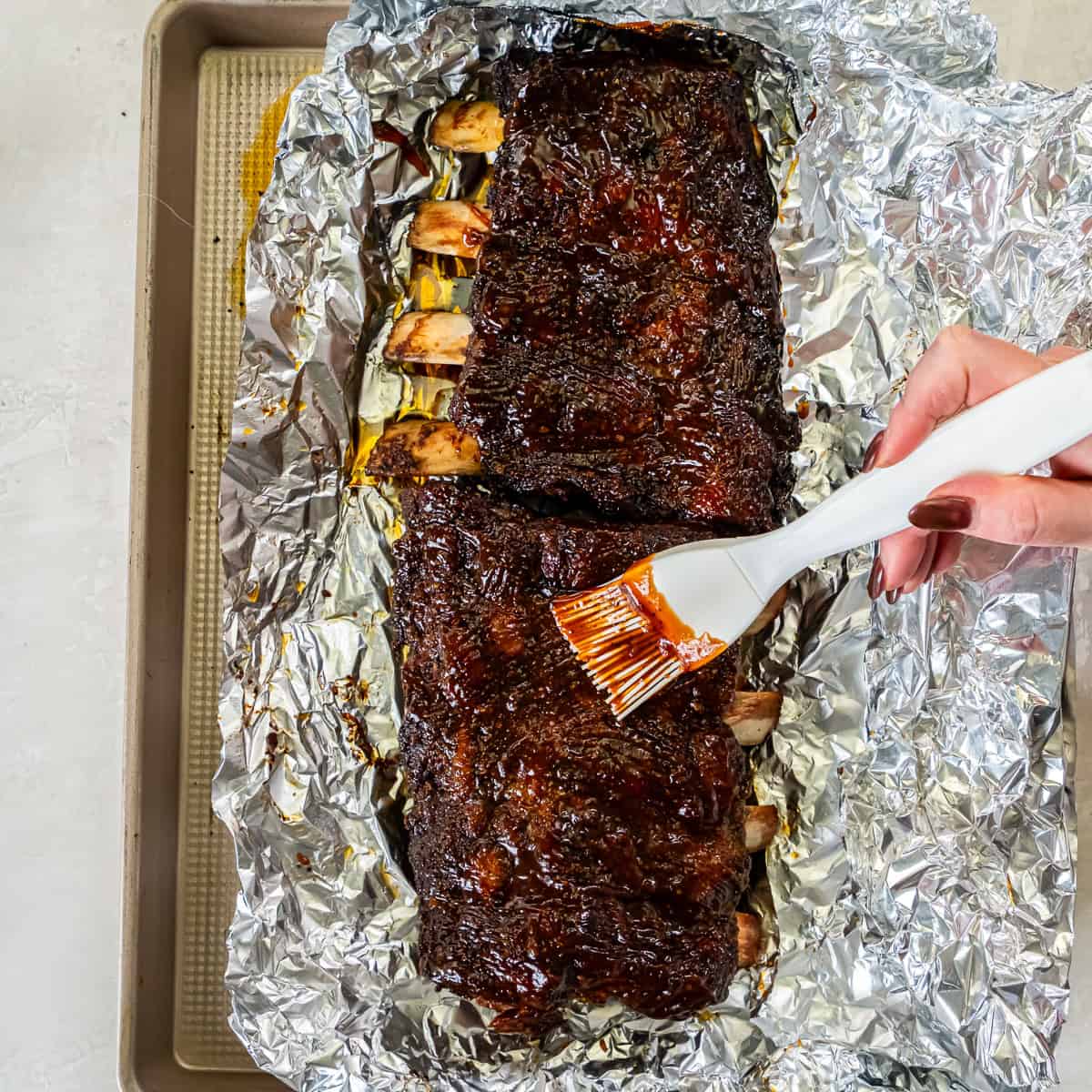 Brushing BBQ sauce over smoked beef back ribs before returning them to the smoker to set the glaze.