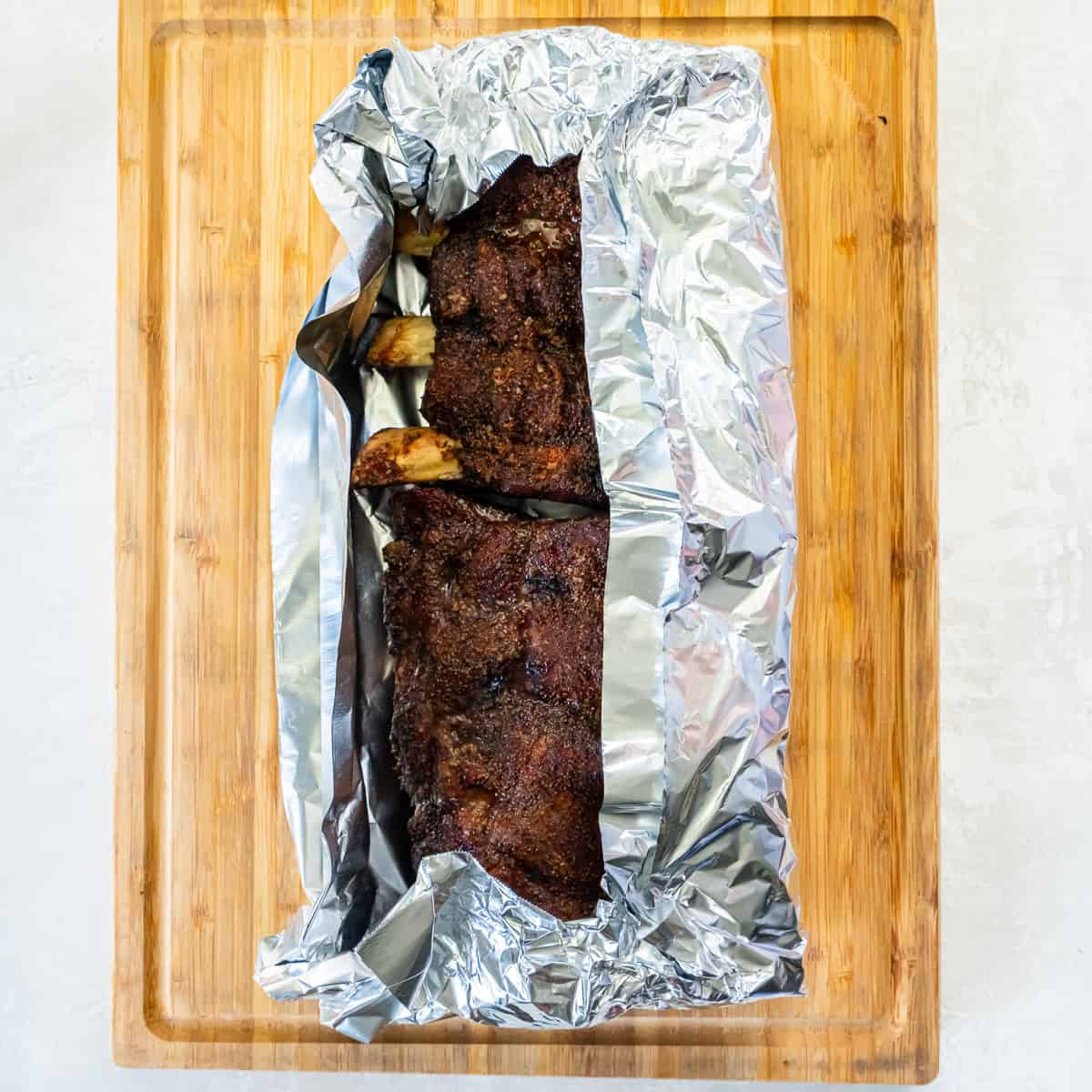 Smoked beef back ribs with a dark bark resting on foil before wrapping and returning to the smoker.