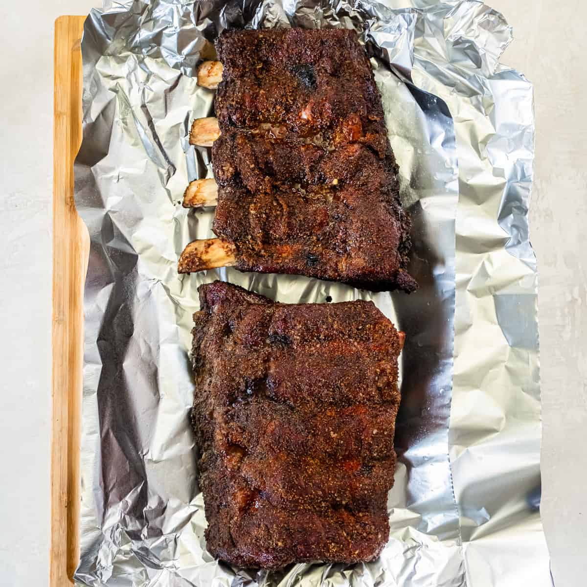 Smoked beef back ribs with a dark bark resting on foil before wrapping and returning to the smoker.