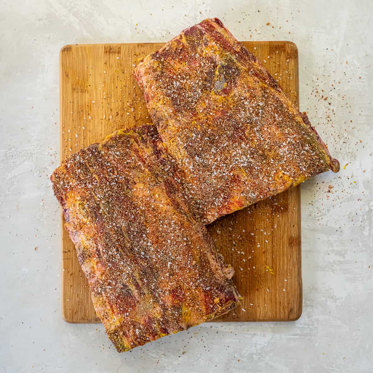 Beef back ribs coated with mustard and seasoned with dry spice rub on a cutting board.