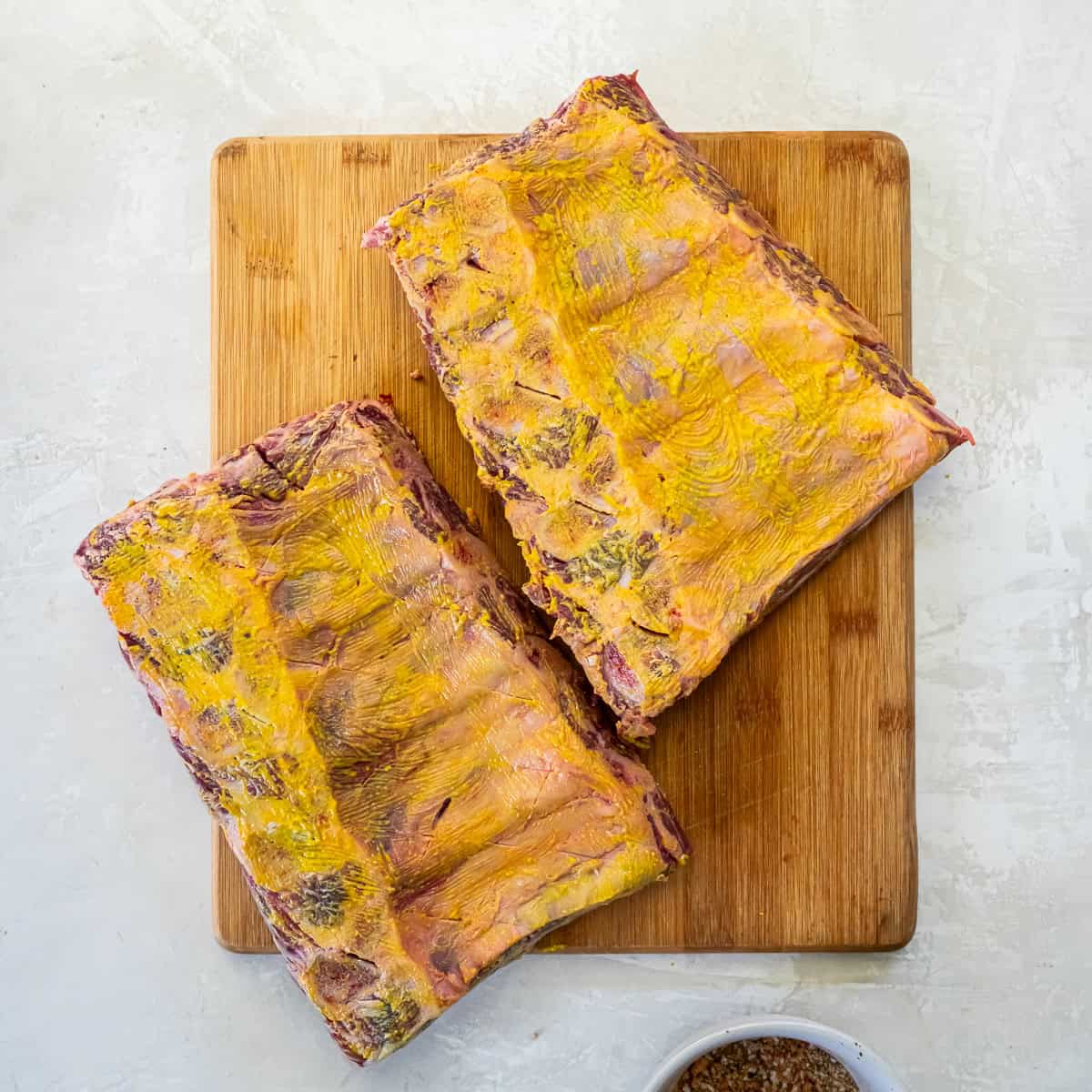 Beef back ribs coated with yellow mustard before adding dry rub seasoning.
