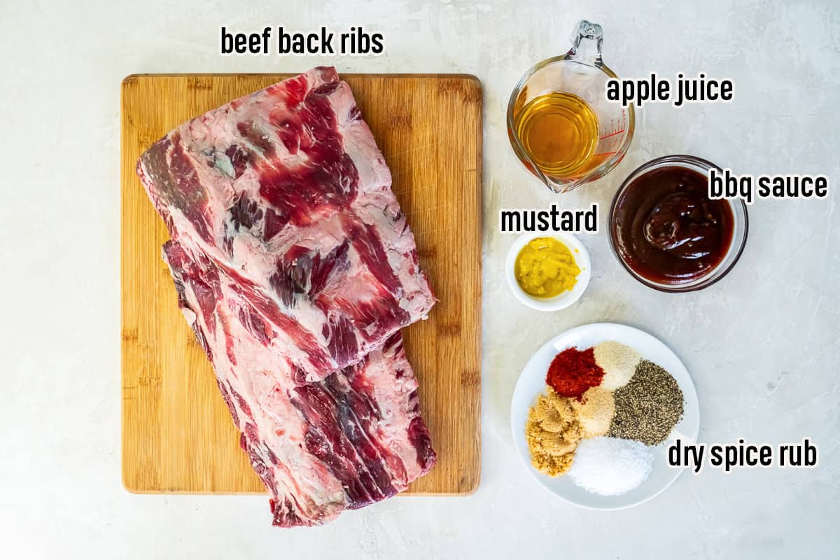 Ingredients for smoked beef back ribs including a rack of beef back ribs, dry spice rub, yellow mustard, apple juice, and BBQ sauce.