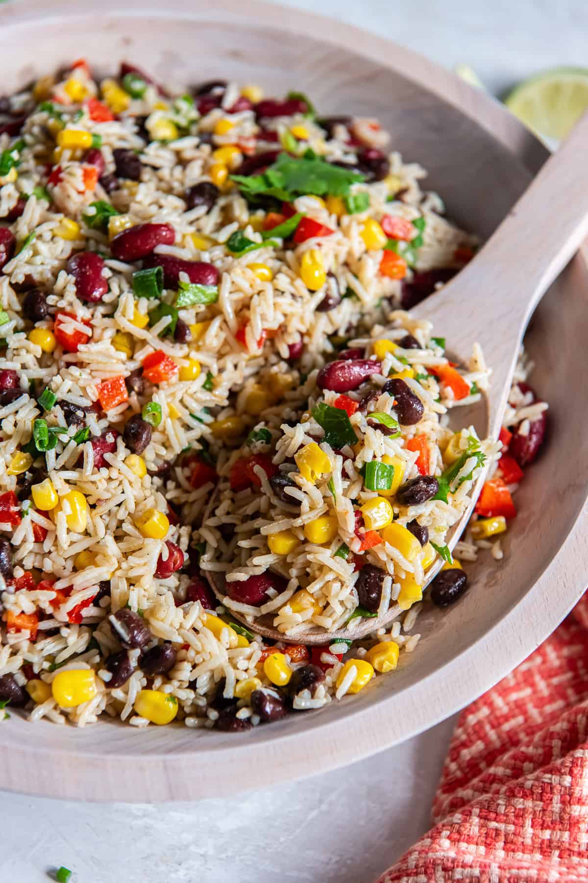 Wooden spoon scooping Tex-Mex Rice and Bean Salad with basmati rice, black beans, kidney beans, corn, and red bell pepper.