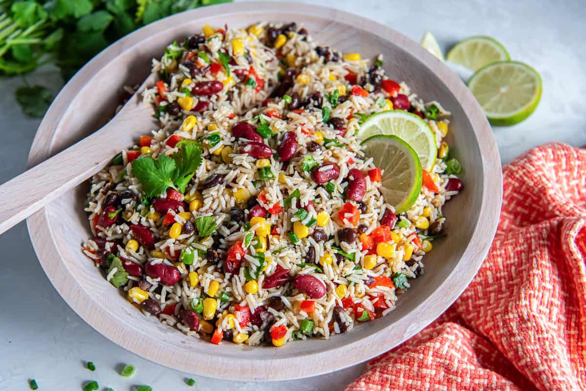 Wooden spoon resting in a bowl of Tex-Mex Rice and Bean Salad with basmati rice, black beans, kidney beans, corn, and red bell pepper.