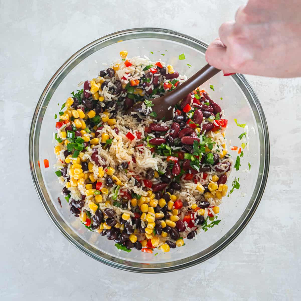 Rice, beans, corn, and vegetables being tossed together with dressing in a large mixing bowl.
