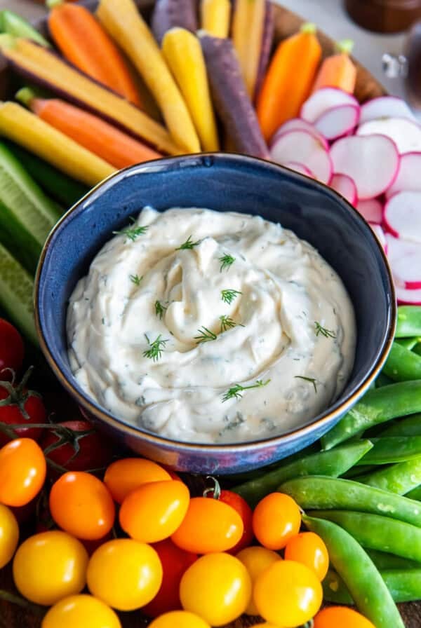 Easy vegetable dip in a bowl surrounded by fresh vegetables including carrots, snap peas, radishes, cucumbers, and cherry tomatoes.
