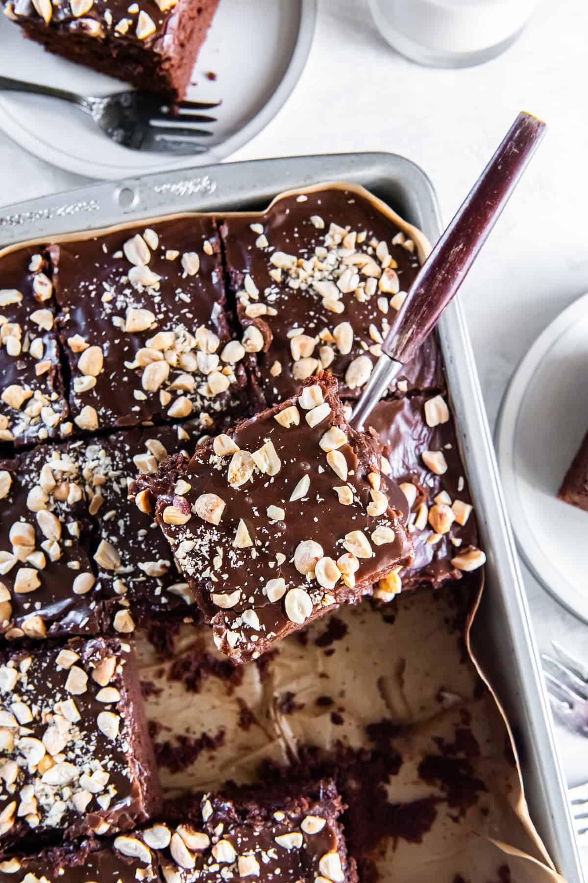 A slice of Chocolate Peanut Butter Cake with fudgy icing and chopped peanuts being lifted from a 13- x 9-inch pan.