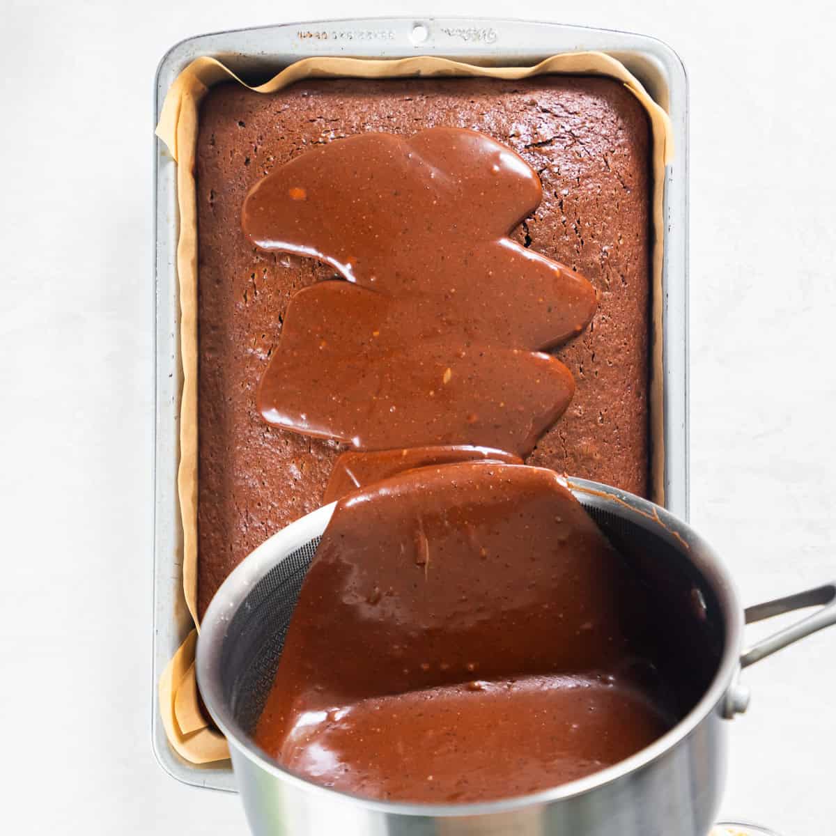 Warm chocolate peanut butter icing being poured over the warm sheet cake.