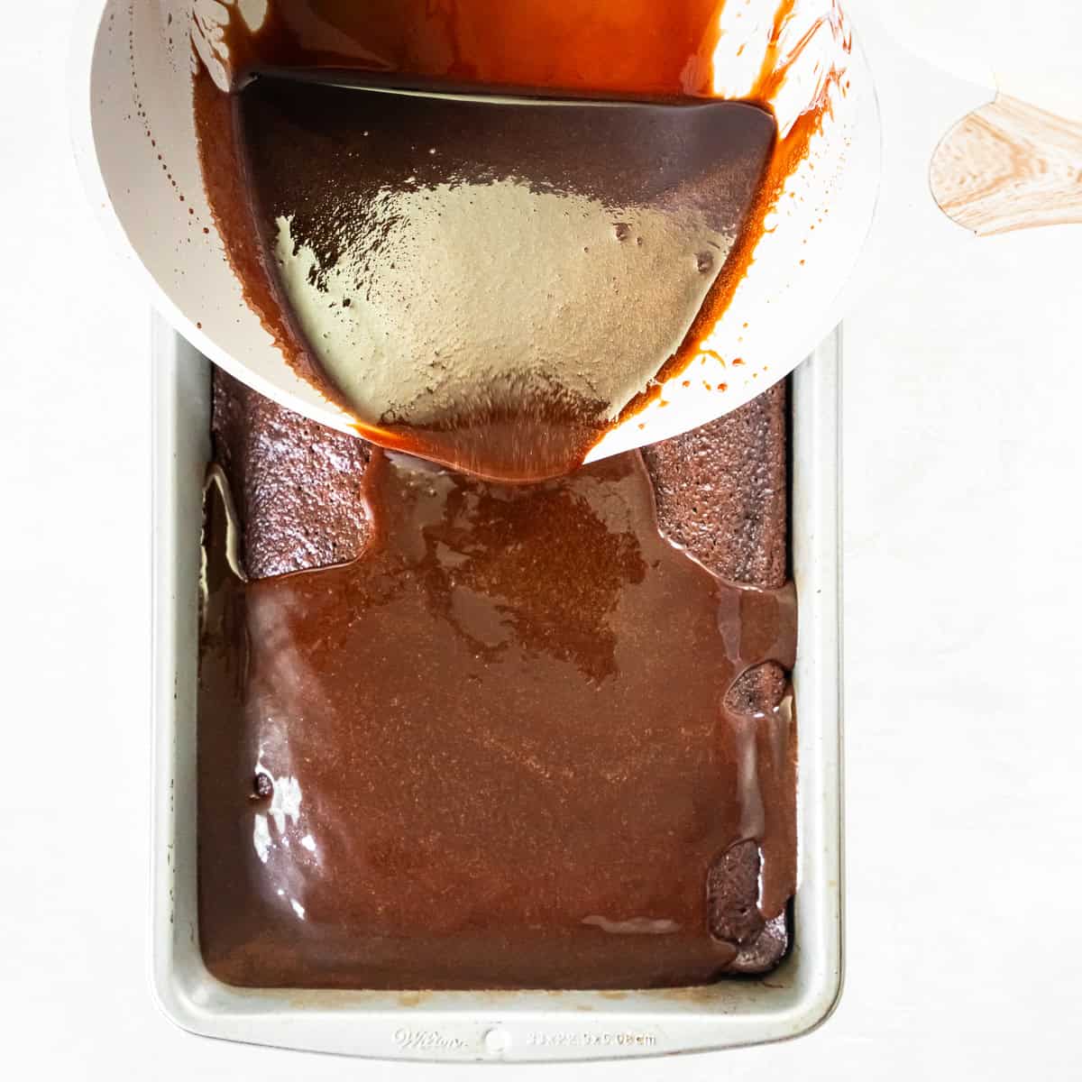 Warm chocolate glaze being poured over freshly baked Coca-Cola Cake.