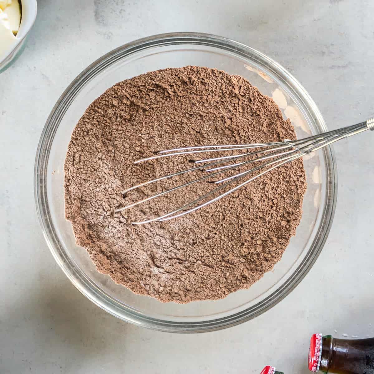 Dry ingredients for Coca-Cola Cake, including flour, sugar, cocoa powder, baking soda, and salt, whisked together in a glass mixing bowl.