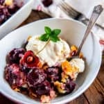 Fresh cherry cobbler topped with vanilla ice cream, a cherry half, and fresh mint in a white bowl.