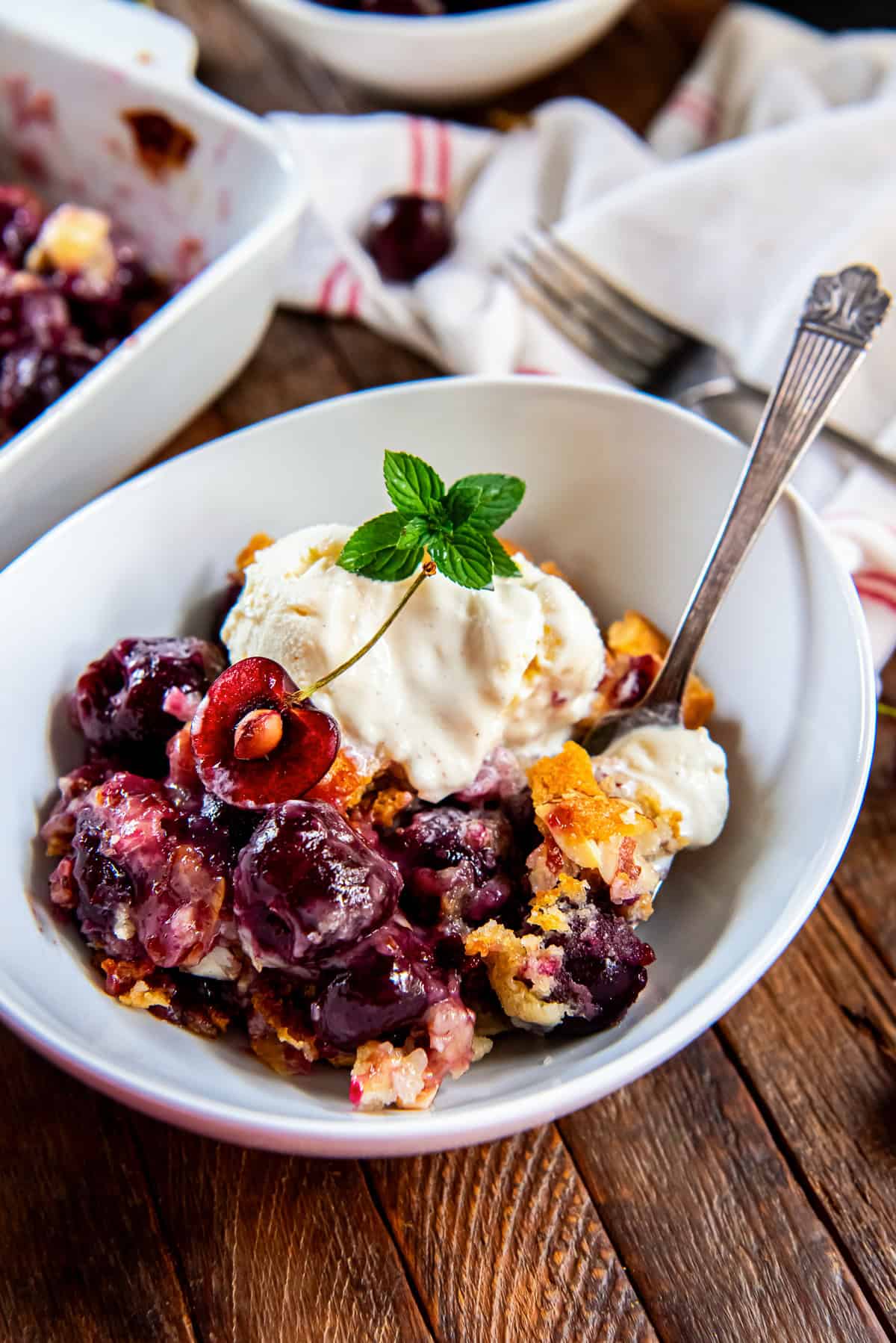 Fresh cherry cobbler served in a white bowl with vanilla ice cream, a cherry half, and fresh mint garnish.