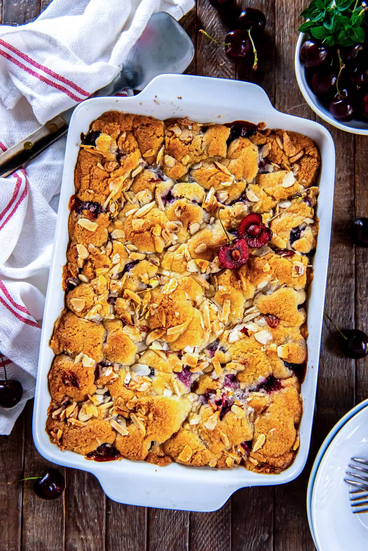Fresh cherry cobbler baked in a white baking dish with a golden biscuit topping, toasted almonds, and sweet cherry filling.
