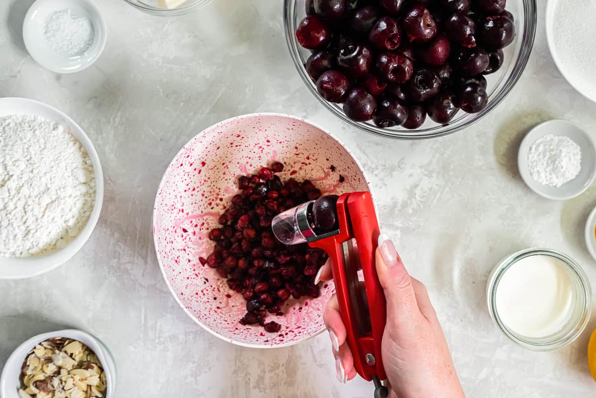 Using a cherry pitter to remove pits from fresh dark sweet cherries for Fresh Cherry Cobbler.