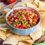 Bowl of fresh tomato salsa with tortilla chips on a wooden serving board.