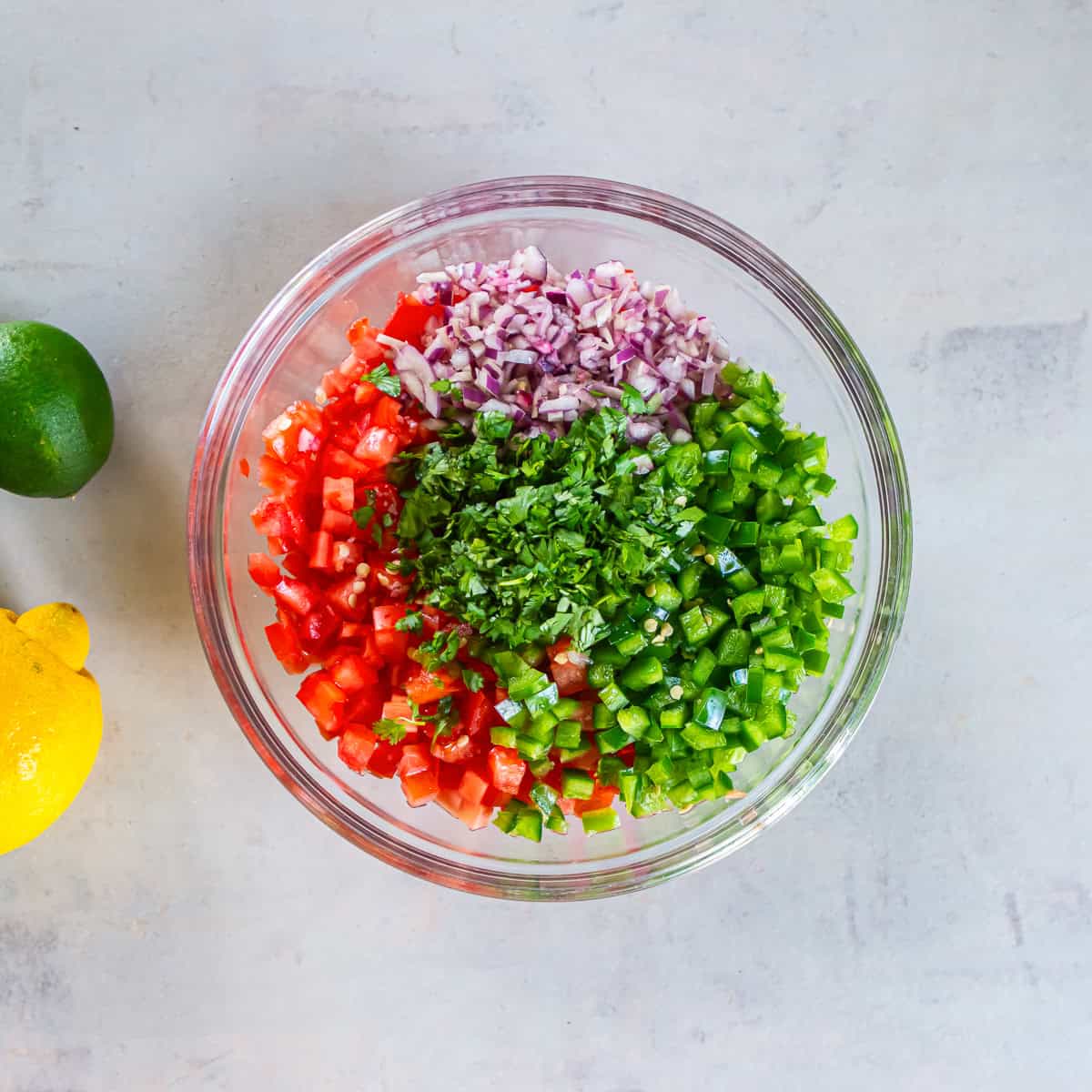 Diced tomatoes, jalapeños, red onion, and chopped cilantro in a glass bowl before mixing to make Fresh Tomato Salsa.