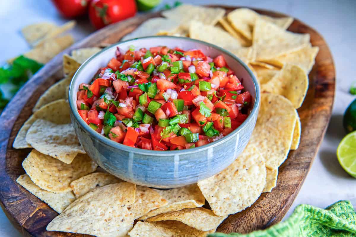 Bowl of fresh tomato salsa with diced tomatoes, jalapeños, red onion, and cilantro served with tortilla chips on a wooden platter.