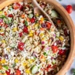 Greek orzo salad with chickpeas, cucumber, tomatoes, bell peppers, olives, feta, and fresh herbs in a wooden serving bowl with a wooden serving spoon.