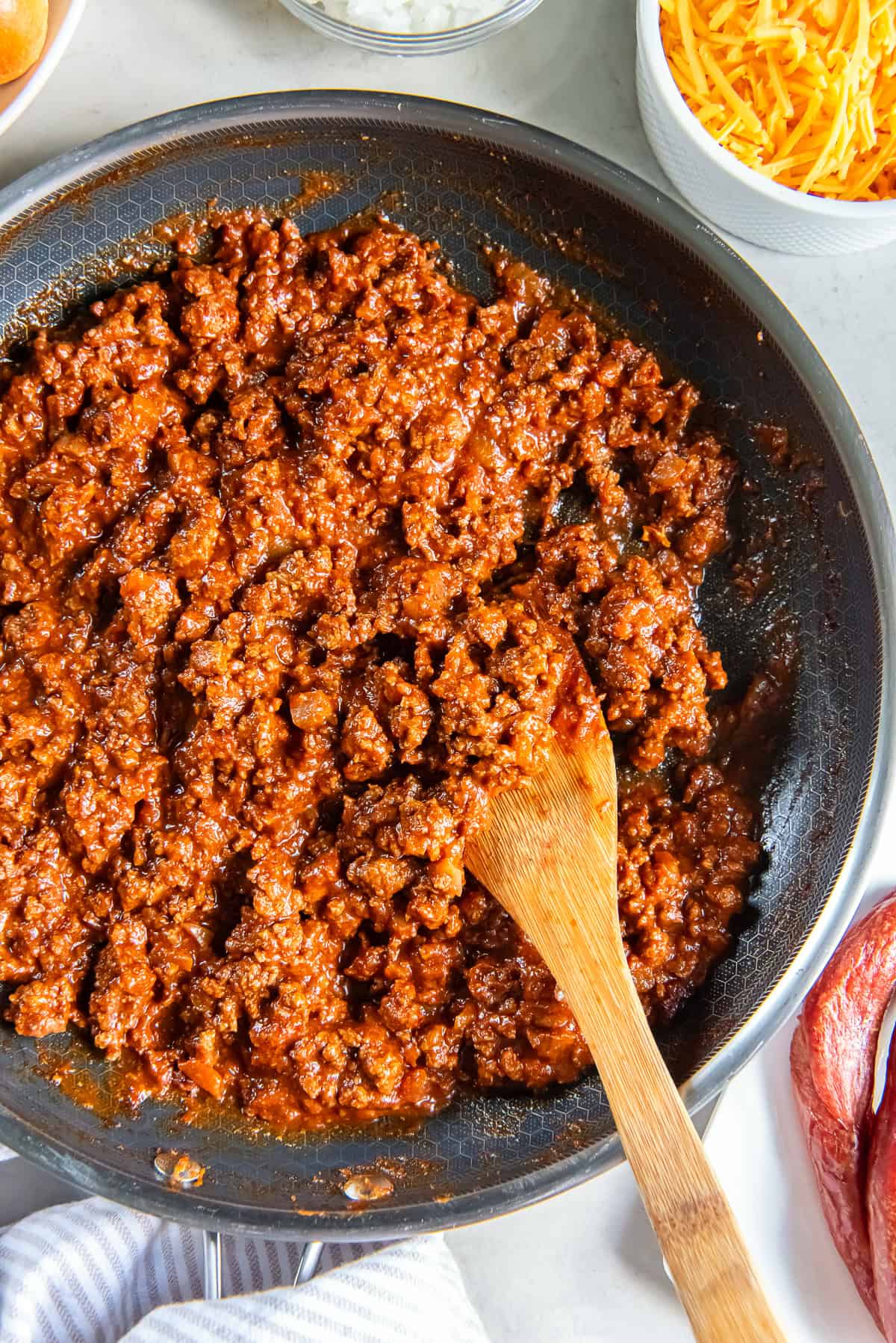 Wooden spoon lifting a scoop of homemade hot dog chili from a skillet, showing the thick ground beef and tomato-based chili used for chili dogs.