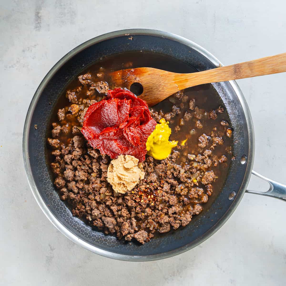 Cooked ground beef and onion in a skillet with tomato paste, beef broth, water, brown sugar, mustard, Worcestershire sauce, and red pepper flakes added.