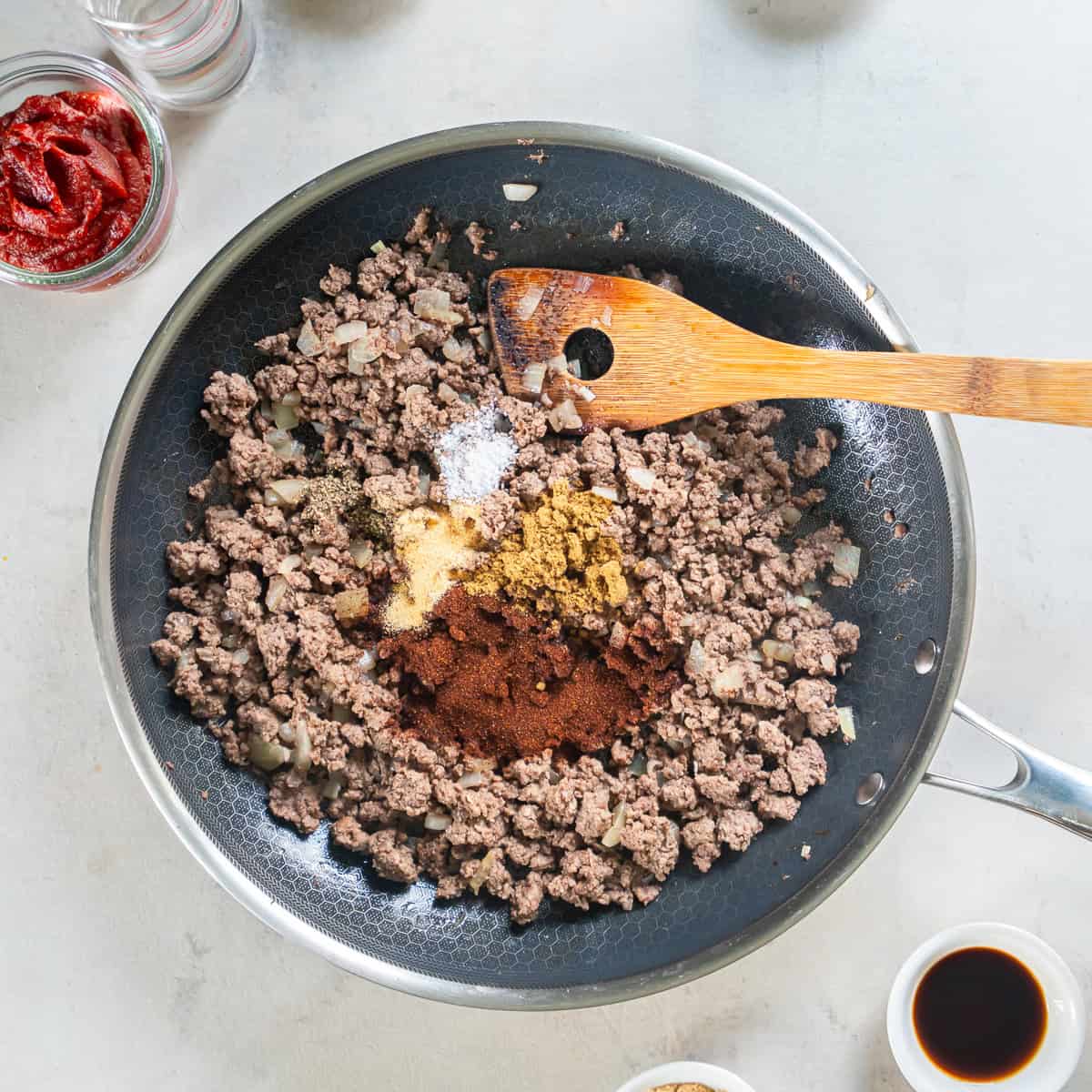 Cooked ground beef and onion in a skillet topped with chili powder, cumin, garlic powder, salt, and pepper.
