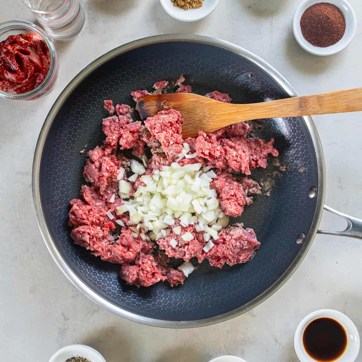 Ground beef and diced onion in a skillet before cooking for homemade hot dog chili.