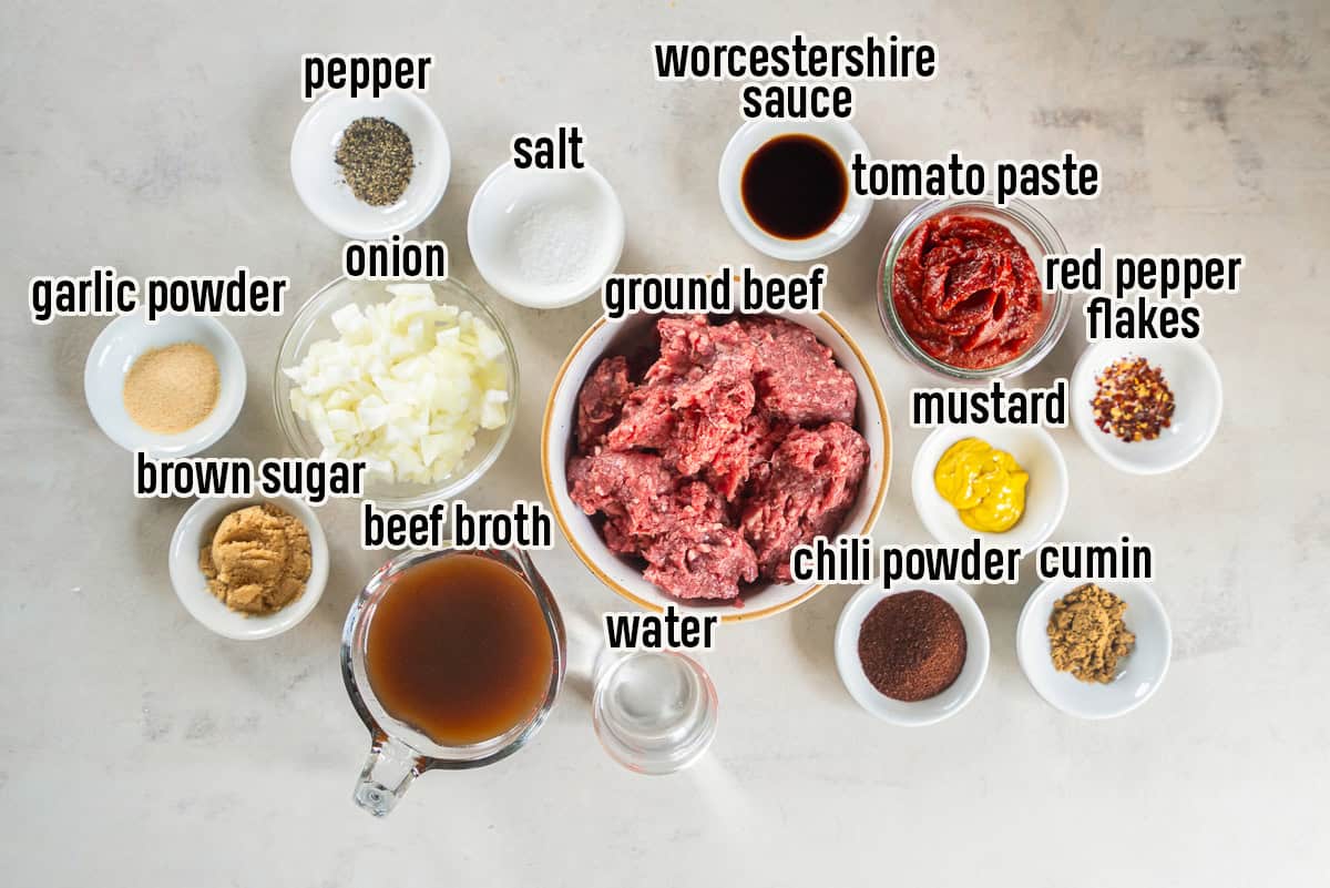 Ingredients for homemade hot dog chili, including ground beef, onion, tomato paste, beef broth, mustard, Worcestershire sauce, chili powder, cumin, garlic powder, brown sugar, and seasonings arranged in labeled bowls