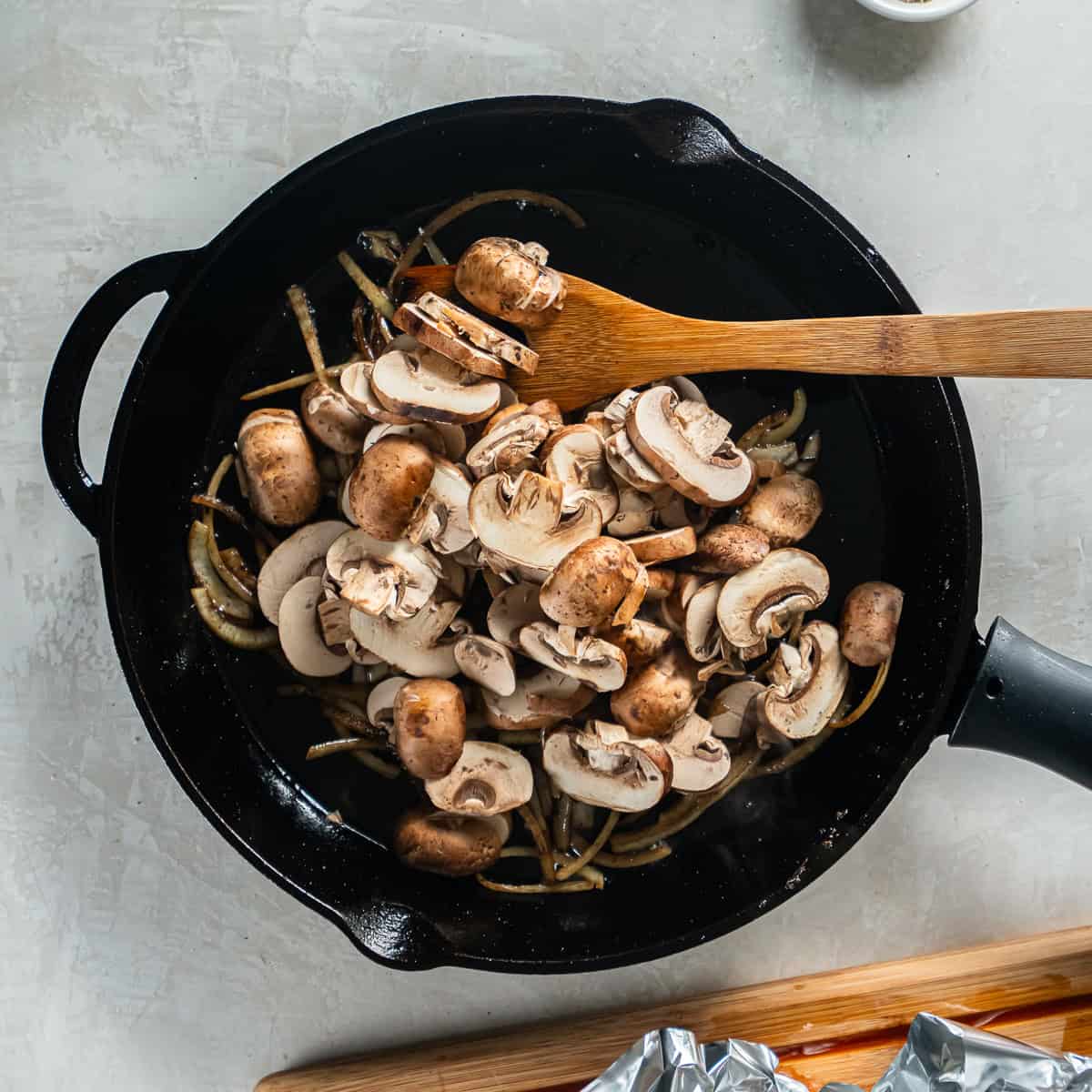 Sliced cremini mushrooms added to onions in a cast iron skillet.