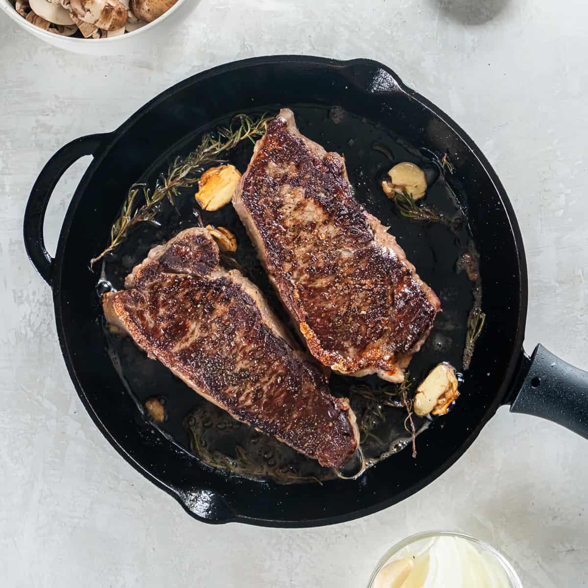 Seared New York Strip Steaks in a cast iron skillet with garlic cloves.