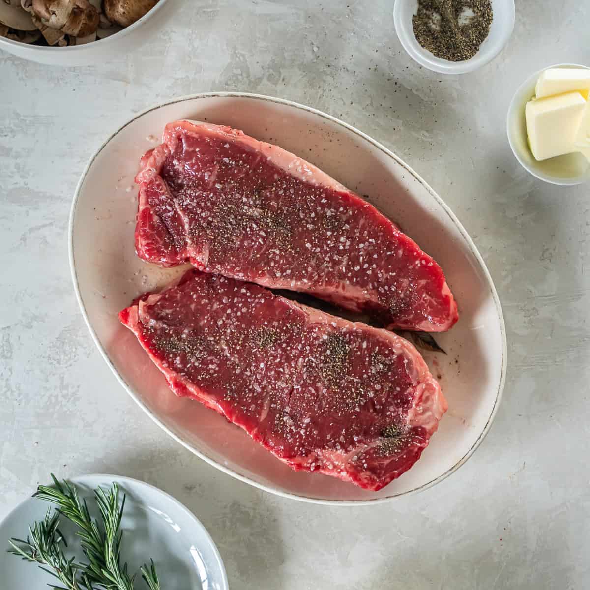 New York strip steaks drizzled with oil and seasoned with kosher salt and black pepper.