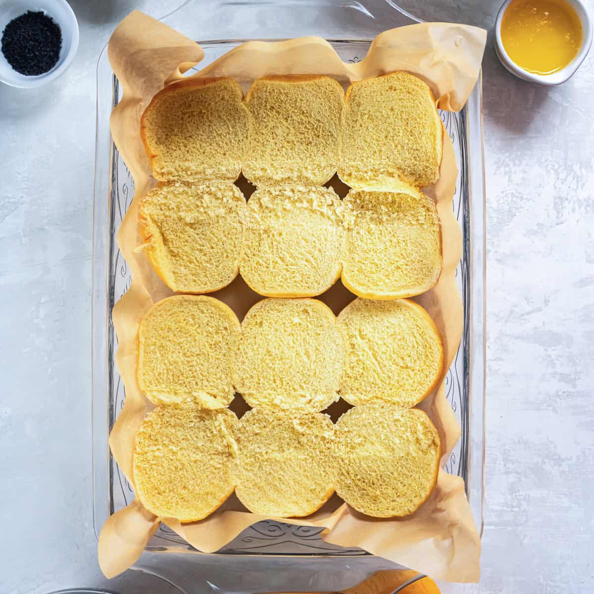 Slider rolls sliced in half and arranged in a parchment-lined baking dish for making pulled pork sliders.