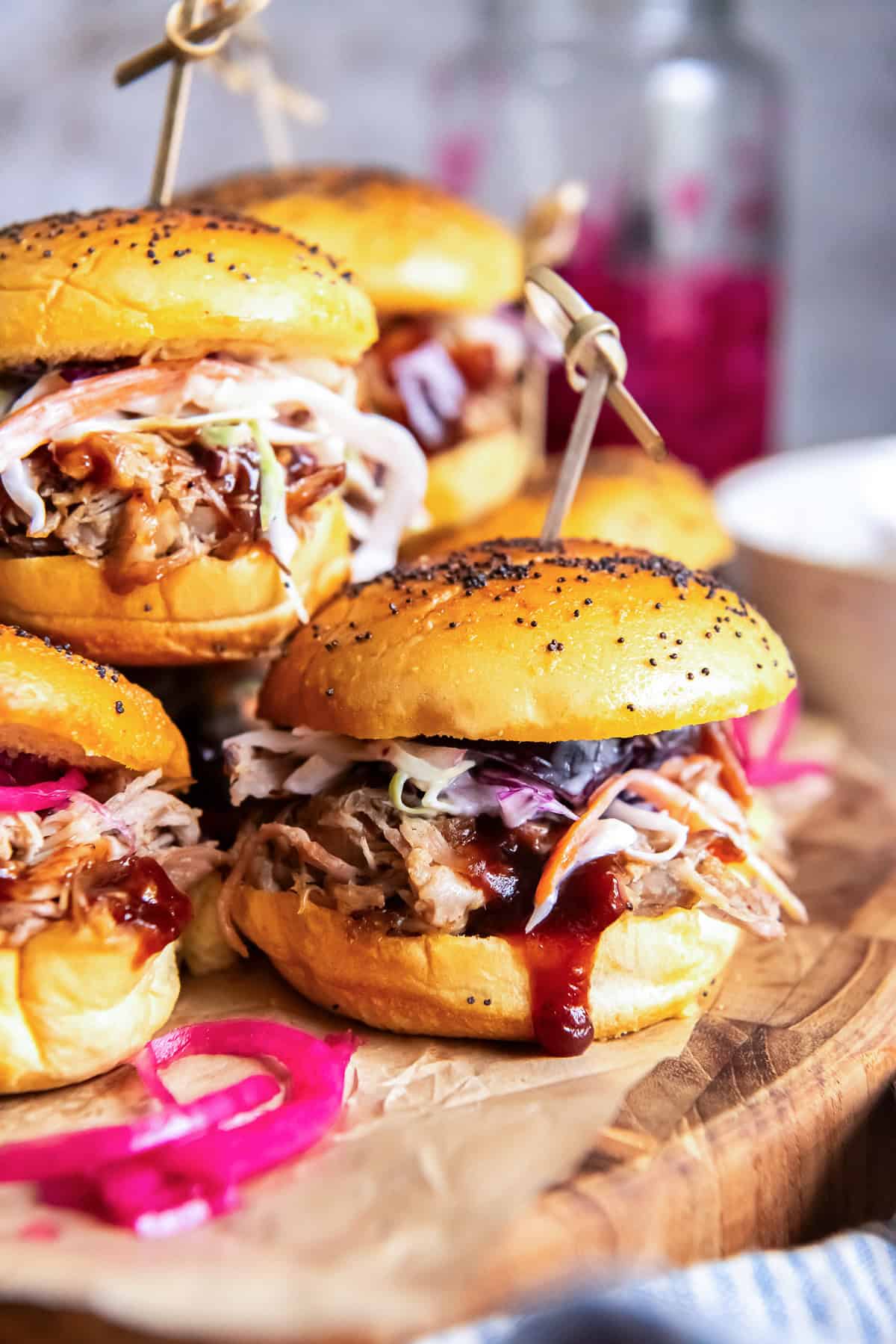 Pulled pork slider topped with creamy coleslaw, barbecue sauce, and pickled red onions on a wooden serving board.