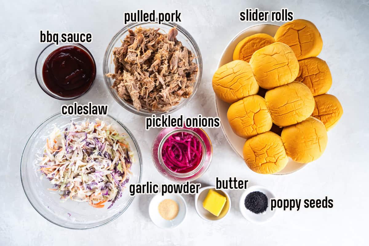Ingredients for pulled pork sliders including slider rolls, slow cooker pulled pork, coleslaw, barbecue sauce, pickled red onions, butter, garlic powder, and poppy seeds.