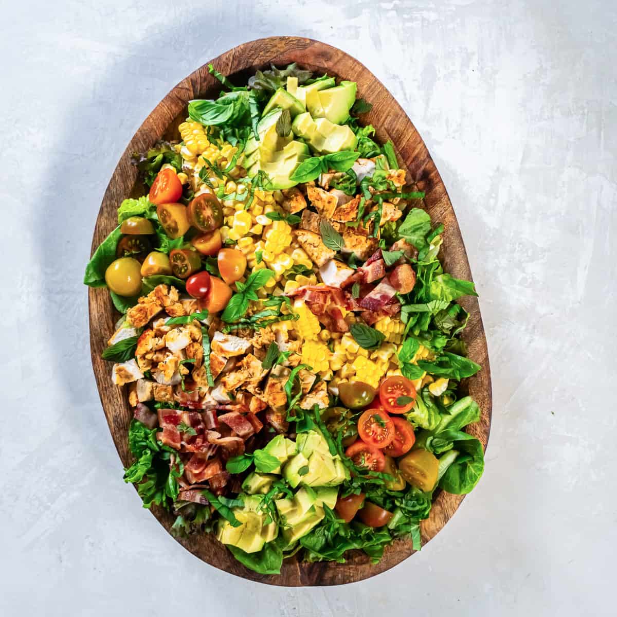 Summer Chicken Salad with bacon, corn, avocado, tomatoes, fresh herbs, and chicken arranged on a serving platter.