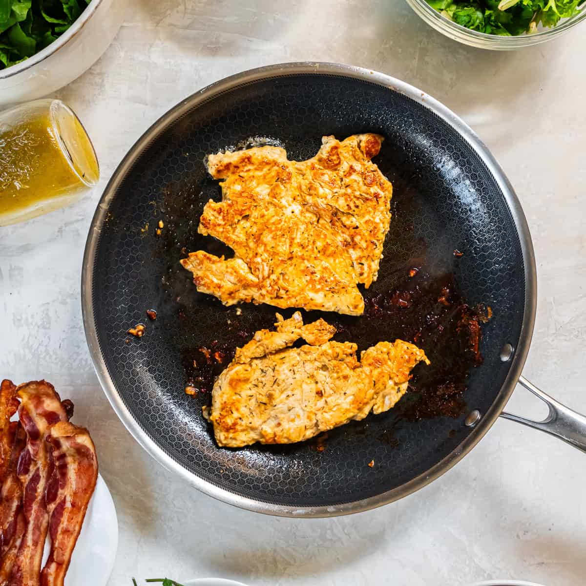 Marinated chicken breasts cooking in a skillet until browned and cooked through.