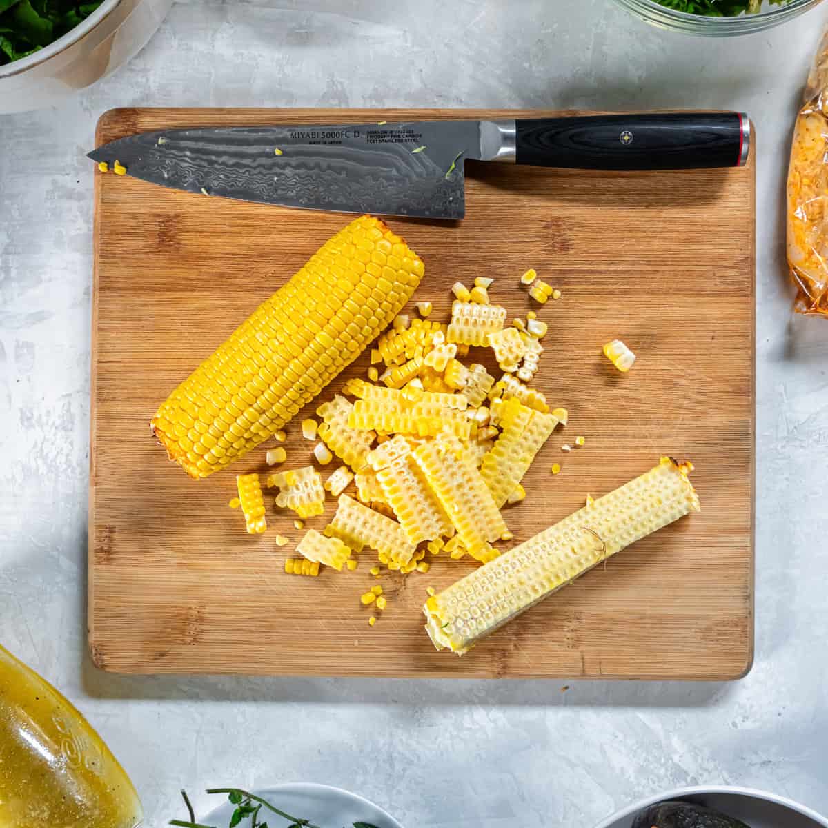 Cutting fresh corn kernels from the cob on a cutting board.