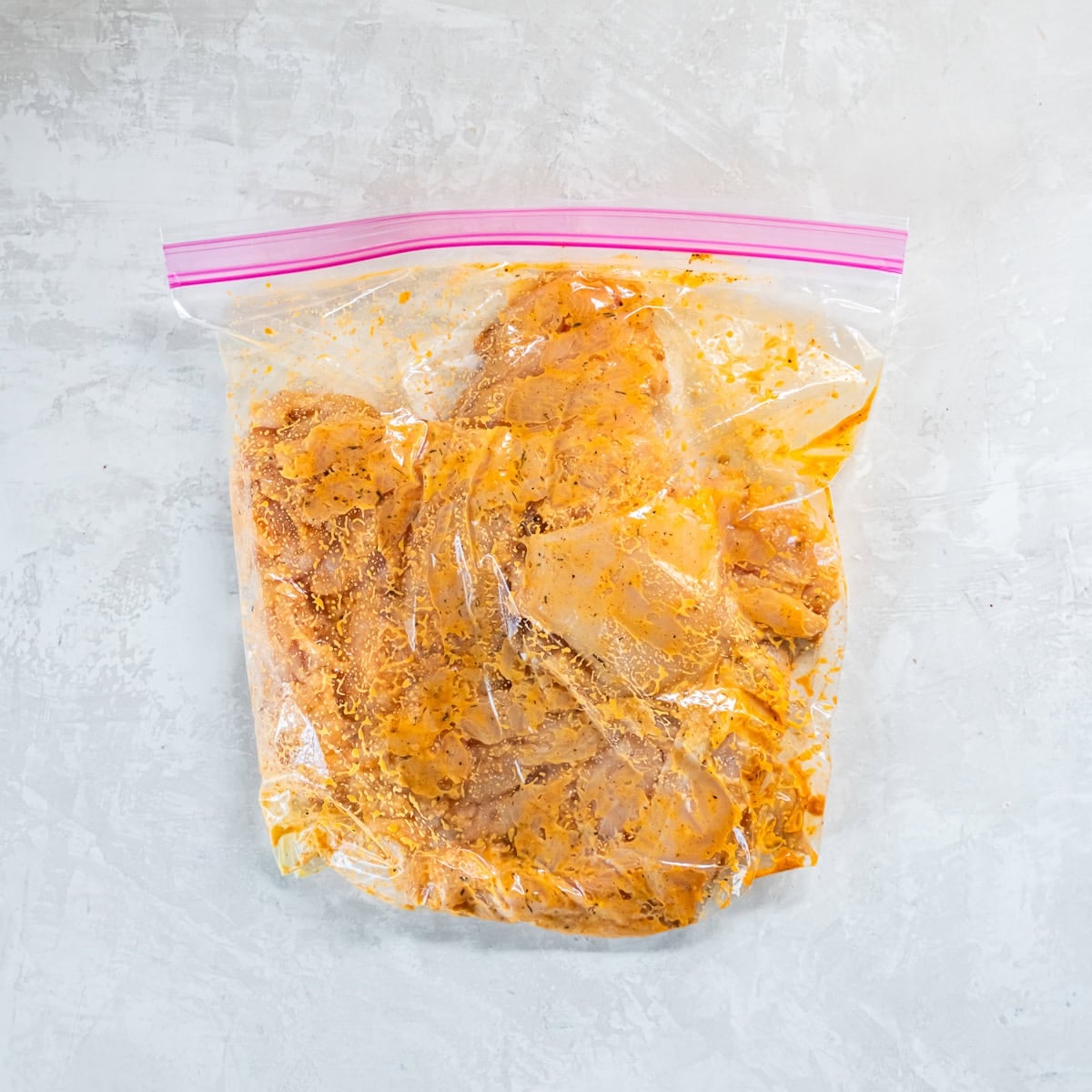 Chicken breasts coated in Cajun marinade in a zip-top bag.