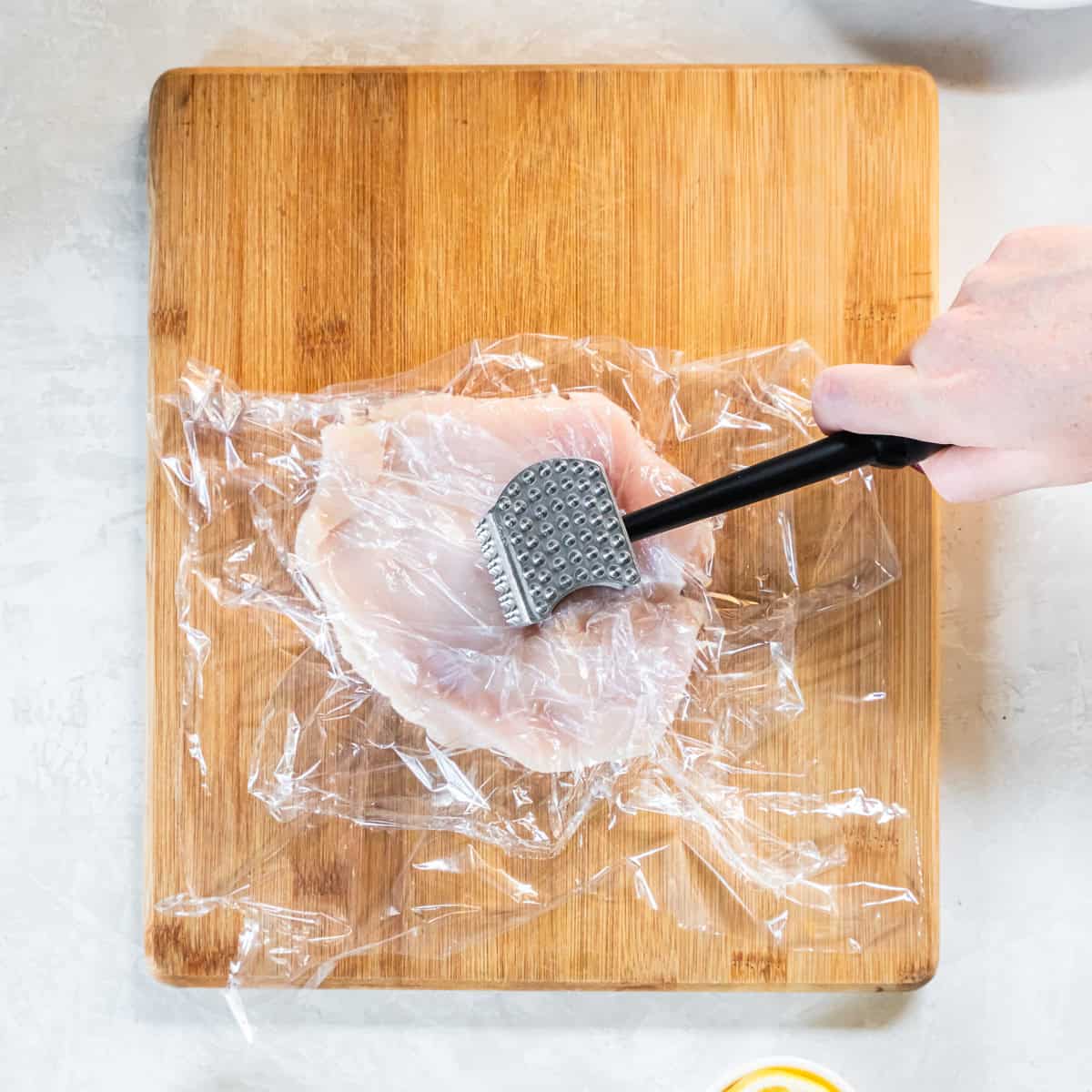 Pounding chicken breasts to an even thickness between sheets of plastic wrap.
