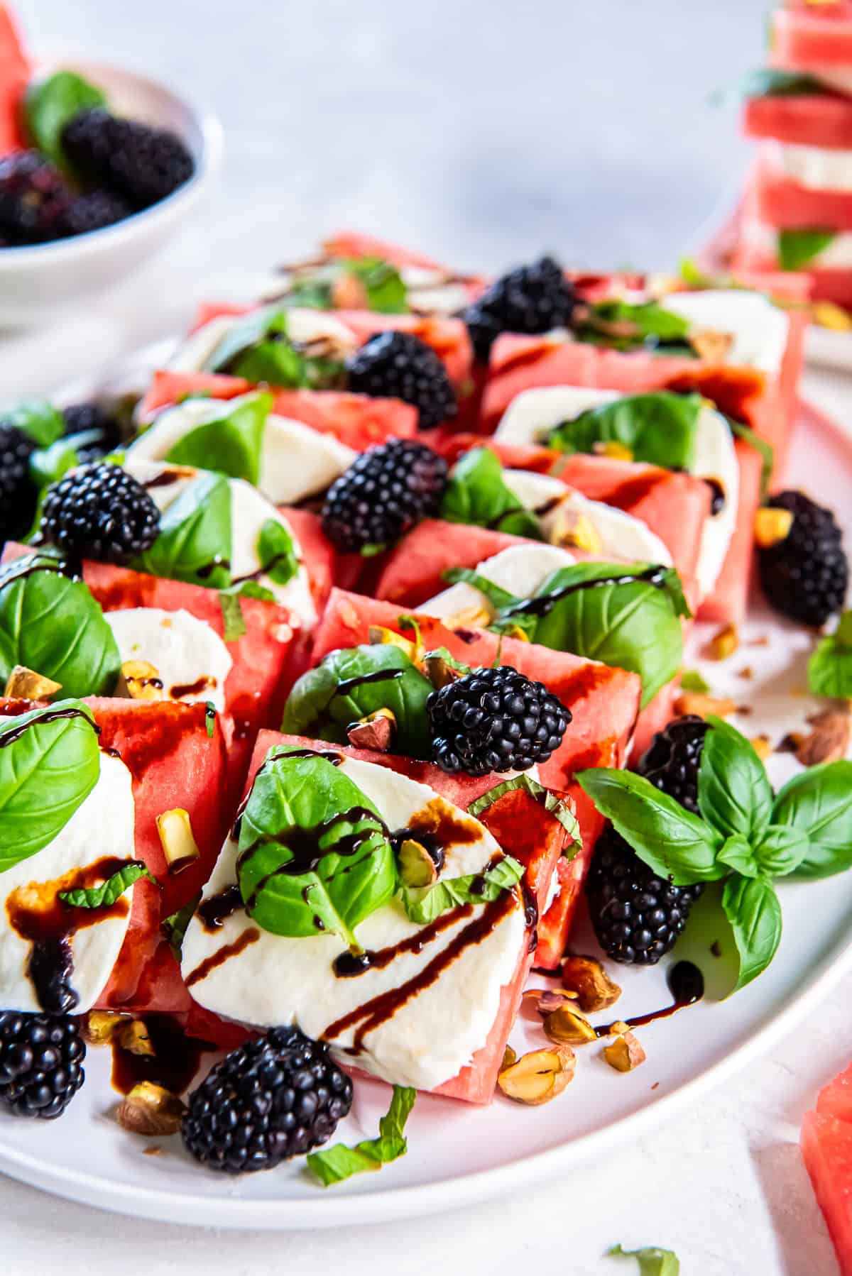 Watermelon Caprese arranged on a serving platter with fresh mozzarella, basil leaves, blackberries, chopped pistachios, and a drizzle of balsamic glaze.