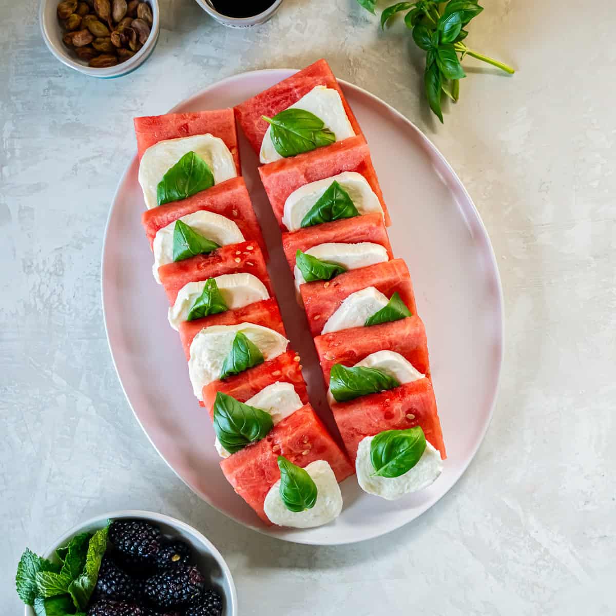 Watermelon squares layered with fresh mozzarella and basil leaves on a serving platter.