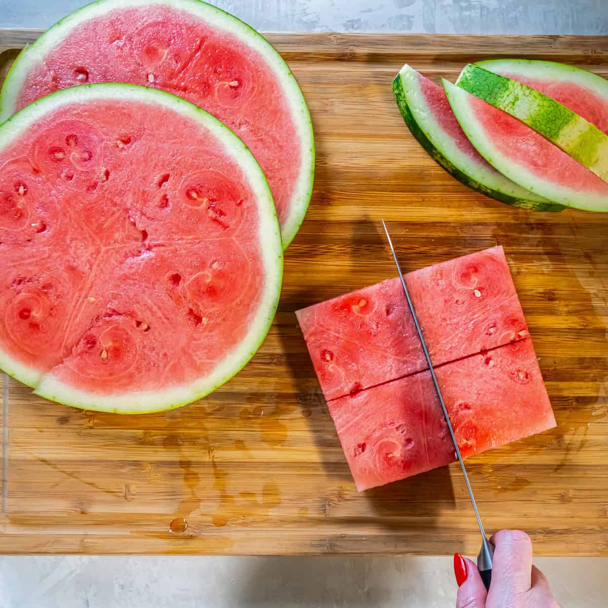 Knife cutting a peeled watermelon slice into squares for watermelon caprese.