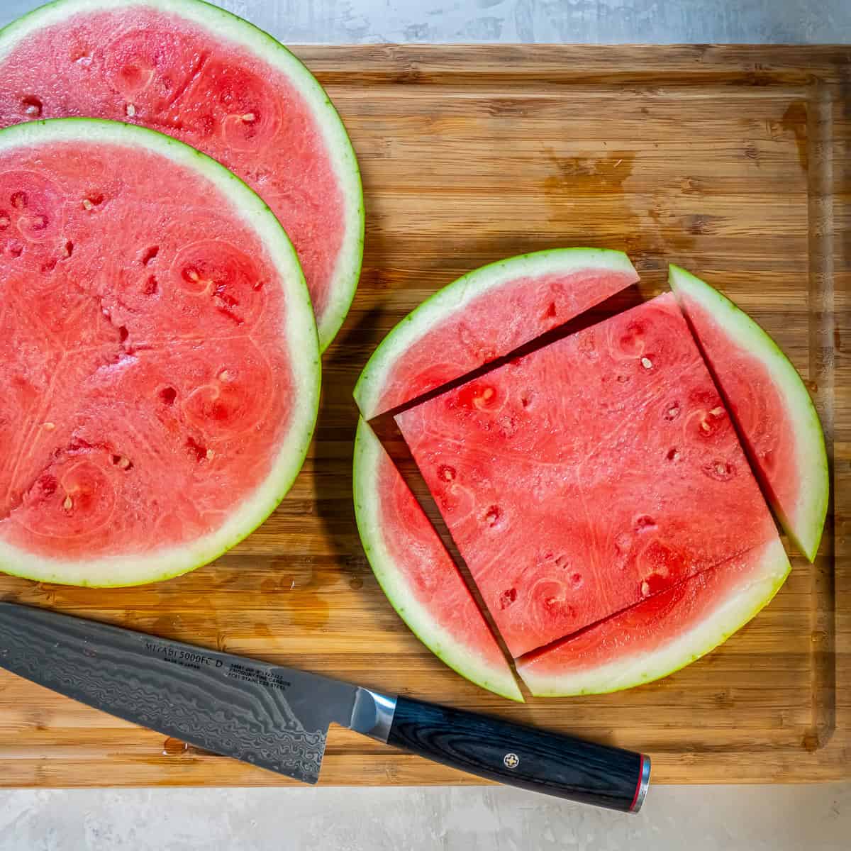 Watermelon slice on a cutting board with the rind trimmed away to create a square piece for watermelon caprese.