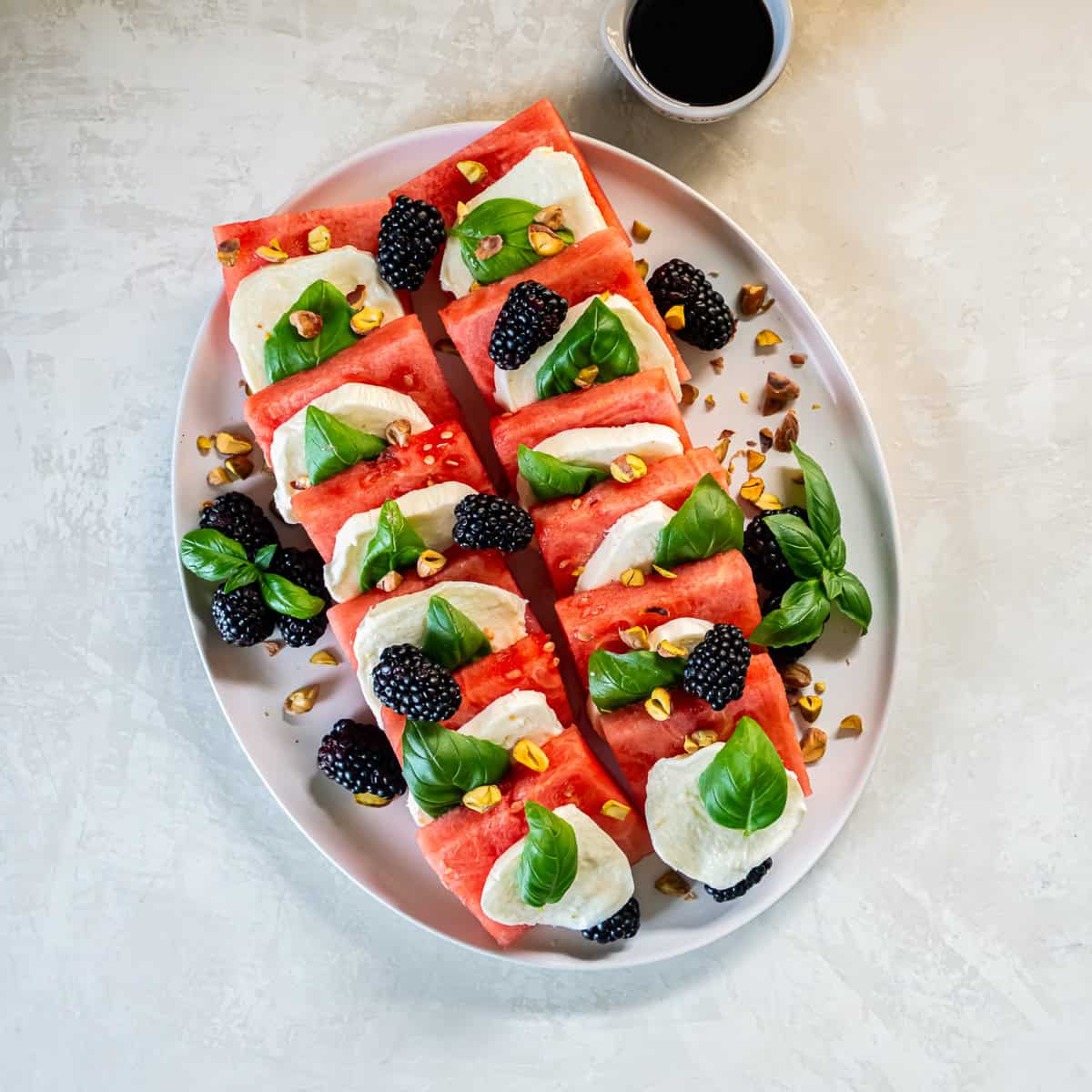 Watermelon caprese topped with blackberries and chopped pistachios before adding balsamic glaze.