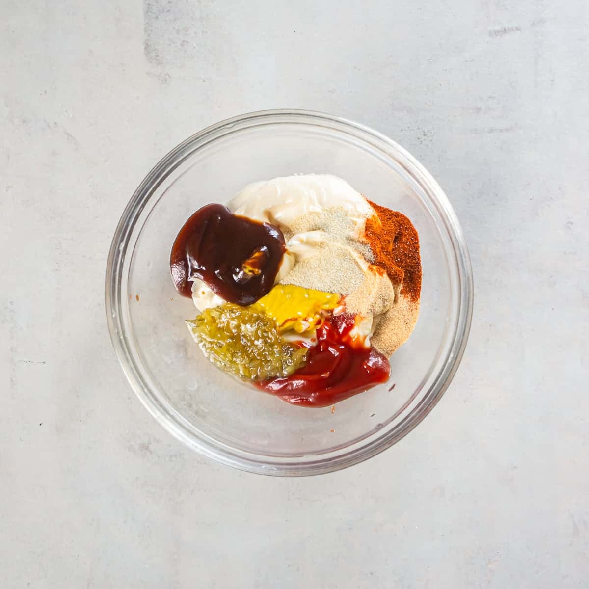 Burger sauce ingredients combined in a glass mixing bowl before stirring.