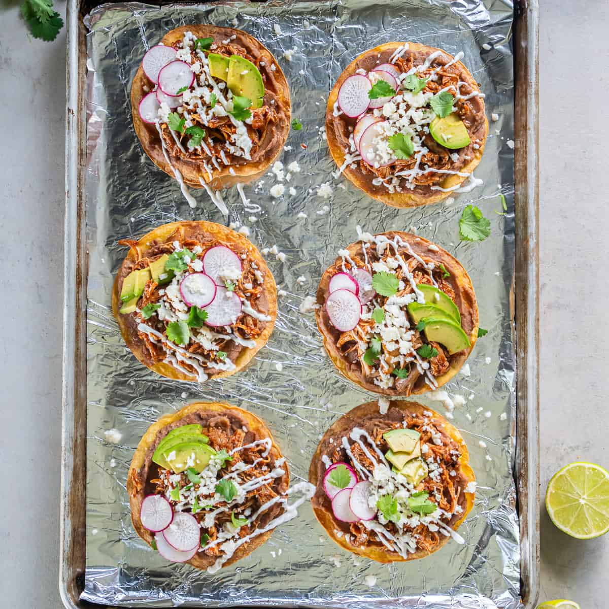 Chicken Tinga Tostadas topped with refried beans, avocado, radishes, Cotija cheese, cilantro, and Mexican crema.