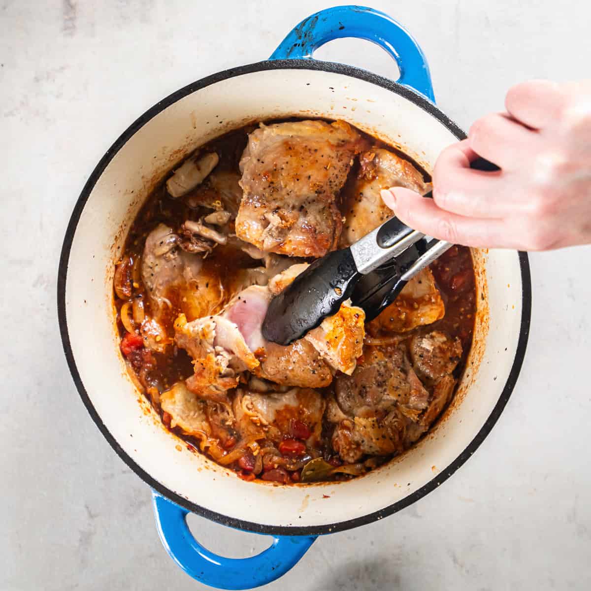 Cooked chicken thighs simmering in chipotle tomato sauce before shredding.