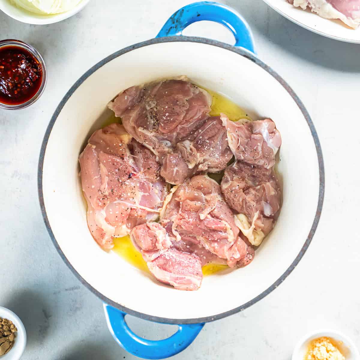 Seasoned chicken thighs browning in olive oil in a Dutch oven.