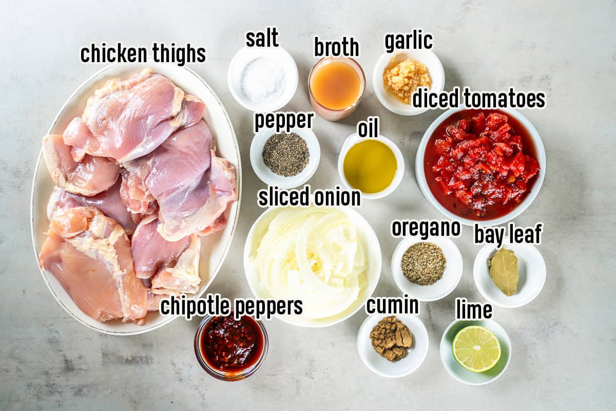 Ingredients for Chicken Tinga including boneless chicken thighs, sliced onion, fire-roasted diced tomatoes, chipotle peppers in adobo, chicken broth, olive oil, garlic, oregano, cumin, bay leaf, lime, salt, and black pepper.