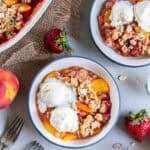 Peach Strawberry Crisp with vanilla ice cream served in bowls next to the baking dish and fresh peaches and strawberries.