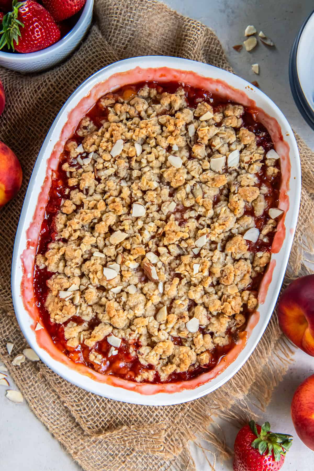 Peach Strawberry Crisp served warm with vanilla ice cream in a bowl, with fresh peaches and strawberries in the background.